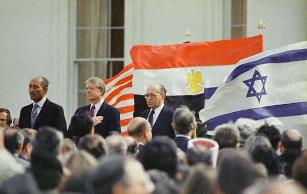 FILE - U.S. President Jimmy Carter, center, Egyptian President Anwar Sadat, left, and Israeli Prime Minister Menachem Begin stand in front of the billowing national flags of the U.S., Egypt and Israel, as the national anthems are played before the signing of the peace treaty between Israel and Egypt at the White House in Washington, March 26, 1979. (AP Photo, File)