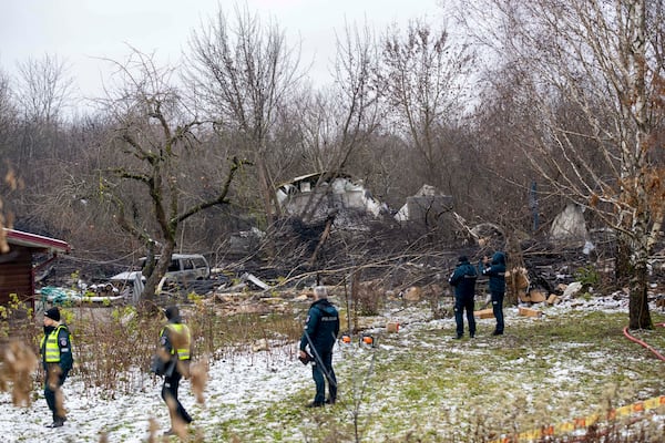 Lithuanian Emergency Ministry employees and police officers stand near the place where a DHL cargo plane crashed into a house near the Lithuanian capital Vilnius, Lithuania, Lithuania, Monday, Nov. 25, 2024. (AP Photo/Mindaugas Kulbis)