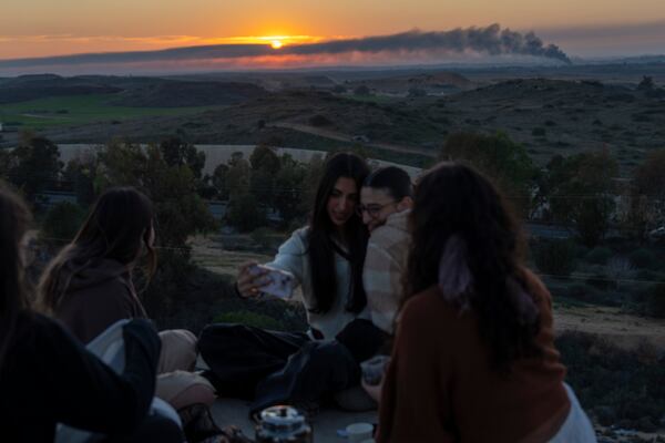 Girls having a selfie in an observation point in Sderot, southern Israel, as smoke rises following an explosion inside the Gaza Strip, Monday, Jan. 13, 2025. (AP Photo/Ariel Schalit)