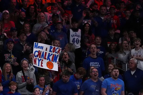 A fan holds a New Year's sign before an NCAA college basketball game between Kansas and West Virginia, Tuesday, Dec. 31, 2024, in Lawrence, Kan. (AP Photo/Charlie Riedel)