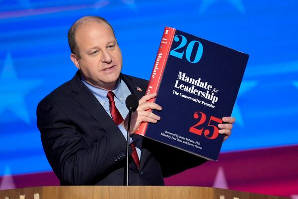 FILE - Colorado Gov. Jared Polis holds up a copy of Project 2025 as he speaks during the Democratic National Convention, in Chicago, Aug. 21, 2024. (AP Photo/J. Scott Applewhite, File)