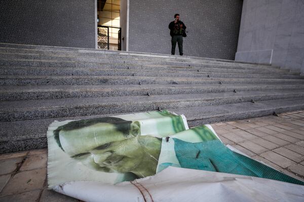 A giant picture of Syrian President Bashar Assad lies on the ground as a Syrian opposition fighter stands nearby, inside the Presidential Palace in Damascus, Syria, Sunday, Dec. 8, 2024. (AP Photo/Omar Sanadiki)