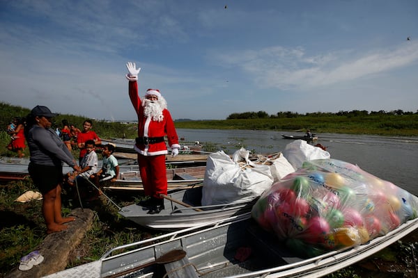 Jorge Barroso, dressed as Santa Claus, waves as he arrives on a boat to distribute Christmas gifts to children who live in the riverside communities of the Amazon, in Iranduba, Brazil, Saturday, Dec. 21, 2024. (AP Photo/Edmar Barros)