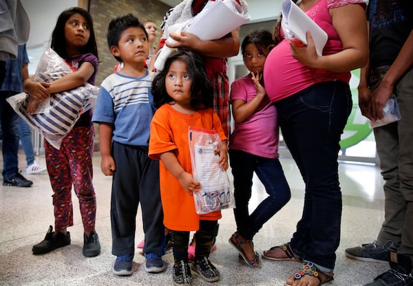 FILE - Ingrid Yanet Lopez Hernandez, 32, center back, her children, from left, Jazmine, 7, Christian, 5, and Cristle Ordonez, 2, and pregnant mother, Meregilda Mejilla, 27, and her daughter, Maricelda Mejilla, 6, wait for transportation to Catholic Charities of the Rio Grande Valley after being processed by the U.S. Border Patrol in McAllen, Texas, on June 24, 2018. (Tom Fox/The Dallas Morning News via AP, File)