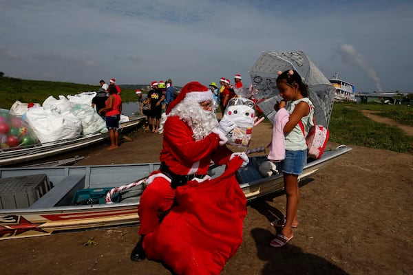 Jorge Barroso, dressed as Santa Claus, presents a gift to a young resident after arriving on a boat to distribute Christmas gifts to children who live in the riverside communities of the Amazon, in Iranduba, Brazil, Saturday, Dec. 21, 2024. (AP Photo/Edmar Barros)