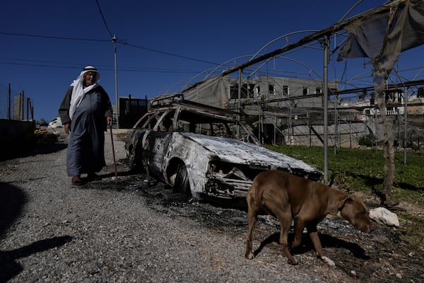 A Palestinian stands beside a torched car in the aftermath of an attack by Israeli settlers in the West Bank village of Jinsafut, Tuesday, Jan. 21, 2025. (AP Photo/Majdi Mohammed)