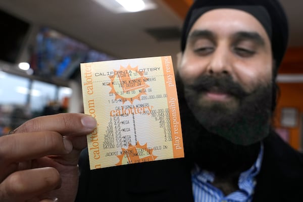 Ishar Gill holds up a copy of the Mega Millions lotto ticket worth an estimated $1.22 billion at his family's store in Cottonwood, Calif., Saturday, Dec. 28, 2024. After three months without anyone winning the top prize in the lottery, the ticket with the winning numbers was drawn Friday night.(AP Photo/Rich Pedroncelli).