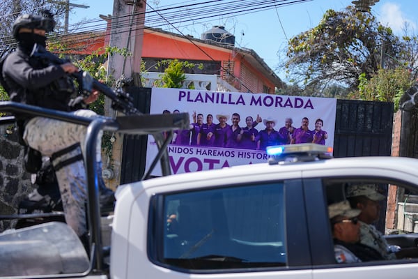 Members of Mexico's National Guard drive past a campaign poster that shows five of the people who were killed the day before, in Huitzilac, Mexico, Tuesday, Jan. 14, 2025. (AP Photo/Fernando Llano)