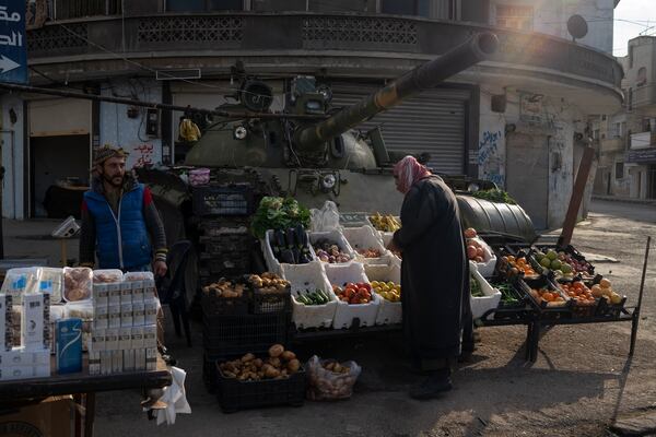 A man looks at fruits and vegetables displayed for sale in front of an ousted Syrian government forces tank that was left on a street in an Alawite neighbourhood, in Homs, Syria, Thursday, Dec. 26, 2024. (AP Photo/Leo Correa)