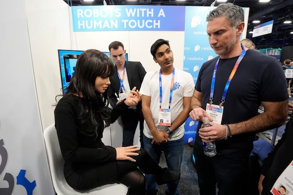 A Realbotix humanoid robot, left, speaks with attendees at a Realbotix booth during the CES tech show Wednesday, Jan. 8, 2025, in Las Vegas. (AP Photo/Abbie Parr)