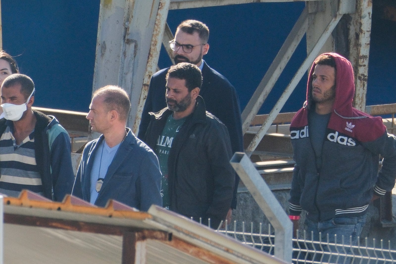 Migrants and security officials walk at the port of Shengjin, northwestern Albania. Wednesday, Oct. 16, 2024 after disembarking from the Italian navy ship Libra, carrying the first group of 16 migrants intercepted in international waters. (AP Photo/Vlasov Sulaj)