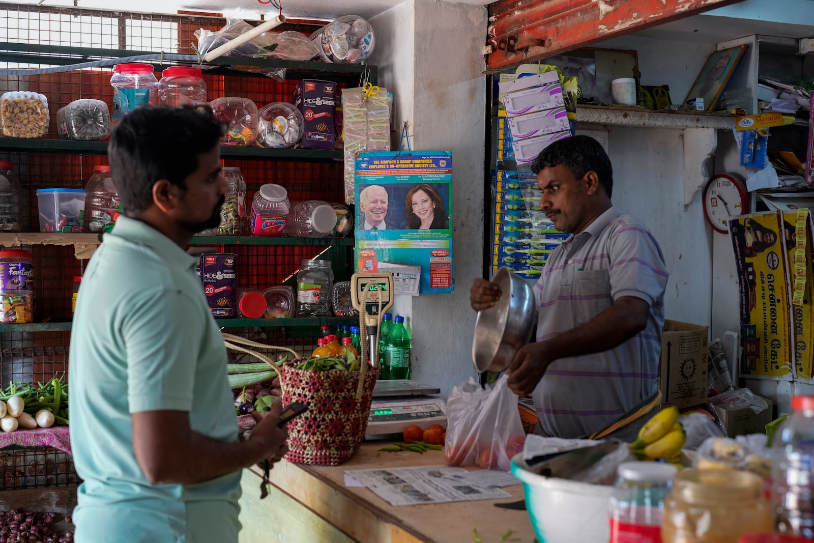 Manikandan Ganesan, right, a local shopkeeper, packs vegetables for a customer at his grocery store outside Sri Dharmasastha Hindu temple in Thulasendrapuram, the ancestral village of Democratic presidential nominee Vice President Kamala Harris, in Tamil Nadu state, India, Monday, Nov. 4, 2024. (AP Photo/Aijaz Rahi)