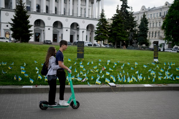 A couple rides a scooter in front of flags honoring soldiers killed fighting Russian troops in Independence Square in Kyiv, Ukraine, Monday, May 23, 2022. (AP Photo/Natacha Pisarenko)