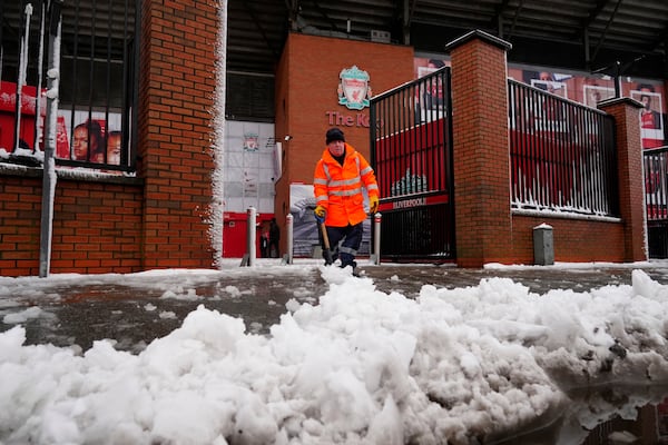 A worker clears snow from a sidewalk in front of the stadium of the premier league soccer club FC Liverpool in Liverpool, England, Sunday, Jan. 5, 2025. (Peter Byrne/PA via AP)