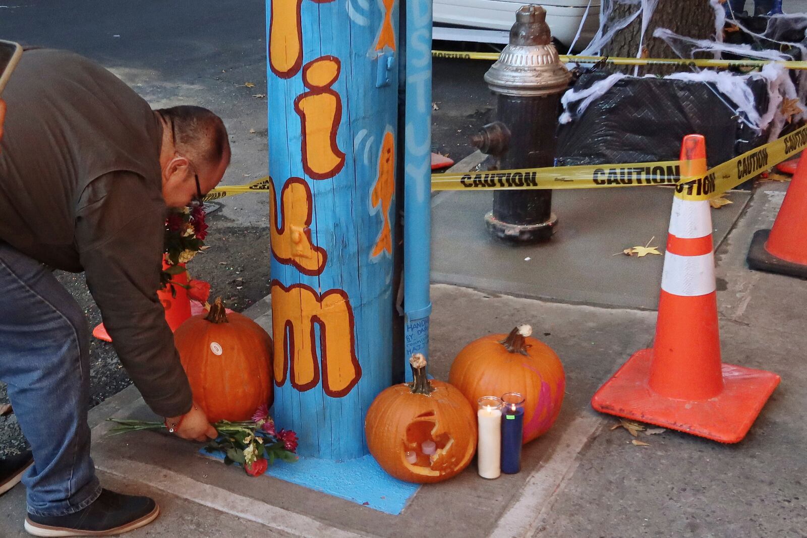 Osvaldo Heredia, of Inland Empire, Calif., places flowers at a makeshift memorial for the Bed-Stuy Aquarium, the yellow caution-taped area around a once leaky fire hydrant that became a makeshift aquarium goldfish pool, and now has been filled with concrete by the city, Friday, Oct. 25, 2024, in the Brooklyn borough of New York. (AP Photo/Cedar Attanasio)