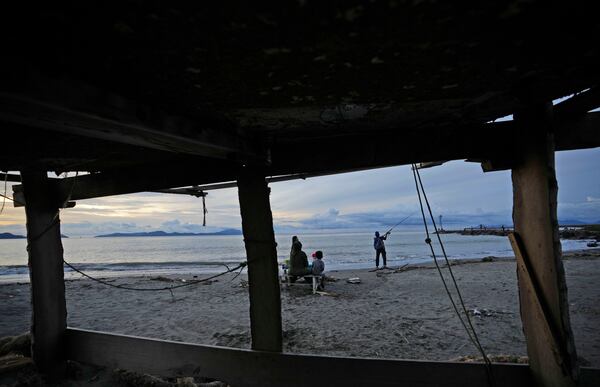 A man fishes as his family looks on in Banda Aceh, Indonesia, Wednesday, Dec. 11, 2024. (AP Photo/Achmad Ibrahim)