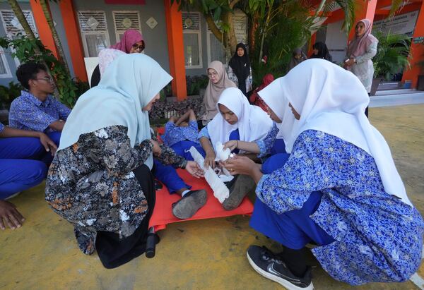 Tria Asnani, left, a 38-year-old teacher who is also a tsunami survivor, assists students to apply splints during an earthquake drill at a school in Banda Aceh, Indonesia, Thursday, Dec. 12, 2024. (AP Photo/Achmad Ibrahim)