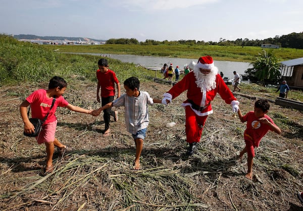 Jorge Barroso, dressed as Santa Claus, is received by young residents after arriving on a boat to distribute Christmas gifts to children who live in the riverside communities of the Amazon, in Iranduba, Brazil, Saturday, Dec. 21, 2024. (AP Photo/Edmar Barros)