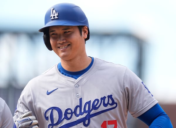 FILE - Los Angeles Dodgers' Shohei Ohtani smiles after reaching first base on a single off Colorado Rockies relief pitcher Seth Halvorsen in the eighth inning of a baseball game Sept. 29, 2024, in Denver. (AP Photo/David Zalubowski, File)