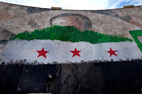 A Syrian boy stands under a giant portrait of the late Syrian President Hafez Assad painted over with the colors of the "revolutionary" flag, in Damascus, Syria, Thursday, Dec. 26, 2024. (AP Photo/Hussein Malla)