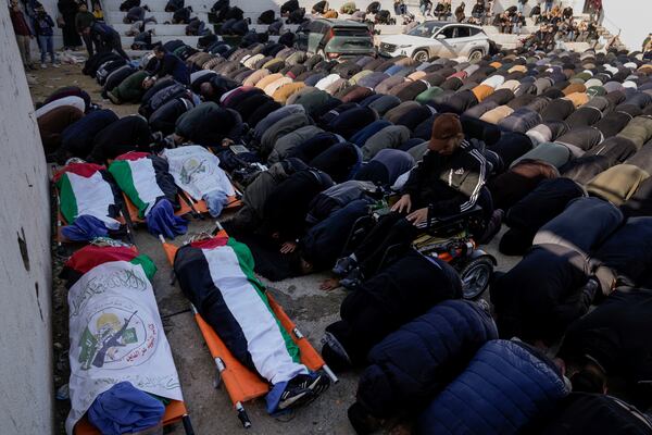 Mourners pray next to the bodies of six Palestinians who were killed in an Israeli airstrike, draped in the Palestinian and Hamas flags during their funeral in Jenin refugee camp, West Bank, on Wednesday, Jan. 15, 2025. (AP Photo/Majdi Mohammed)