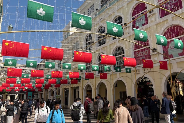 Tourists walk past a street decorated with Chinese national flags and Macao regional flags in Macao on Dec. 13, 2024. (AP Photo/Kanis Leung)