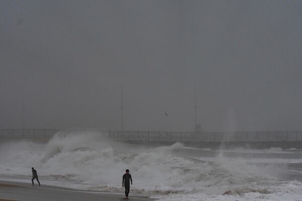 Two surfers walk along the beach as waves crash in Seal Beach, Calif., Tuesday, Dec. 24, 2024. (AP Photo/Jae C. Hong)