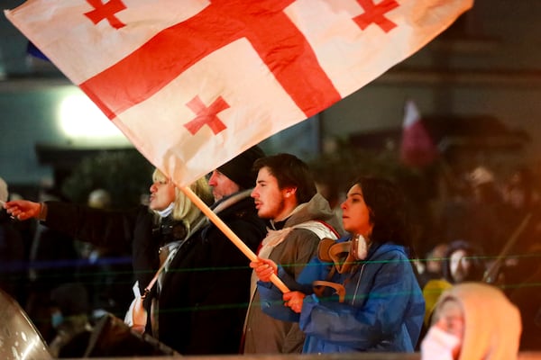 One of demonstrators holds a Georgian national flag in front of police who blocked a street to prevent protesters rallying against the governments' decision to suspend negotiations on joining the European Union for four years, outside the parliament's building in Tbilisi, Georgia, early Saturday, Nov. 30, 2024. (AP Photo/Zurab Tsertsvadze)