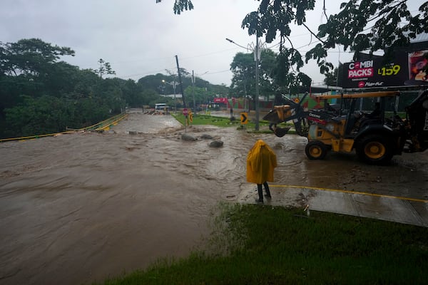 A worker stands alongside an overflowing river flooded by rains brought on by Tropical Storm Sara in San Pedro Sula, Honduras, Saturday, Nov. 16, 2024. (AP Photo/Moises Castillo)