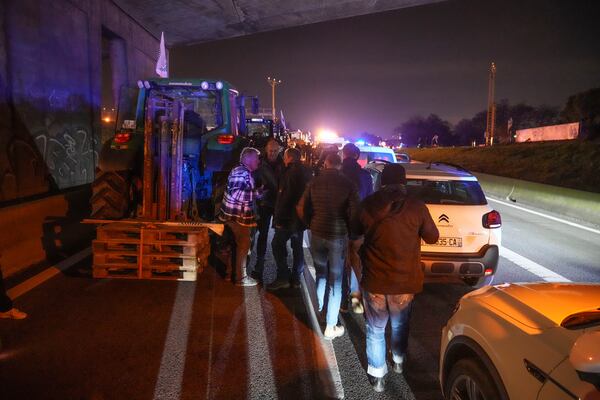 Farmers walk between tractors and cars on a blocked highway in Velizy-Villacoublay, outside Paris, Sunday Nov. 17, 2024. (AP Photo/Michel Euler)