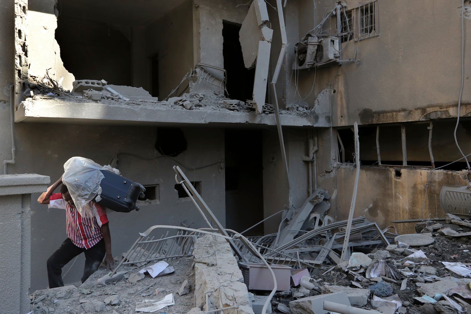 A man carries a luggage as he walks on the rubble of destroyed apartments that were hit by Israeli airstrikes, in Tyre, south Lebanon, Thursday, Oct. 24, 2024. (AP Photo/Mohammed Zaatari)