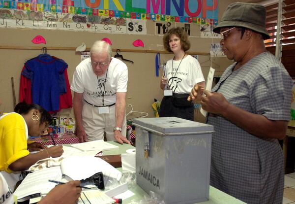 FILE - Former U.S. President Jimmy Carter, second left, and Jennifer McCoy, third left, observe the voting process, while Joyce Grey, right, waits to cast her ballot at a polling station in Kingston, Jamaica, Oct. 16, 2002. (AP Photo/Andres Leighton, File)