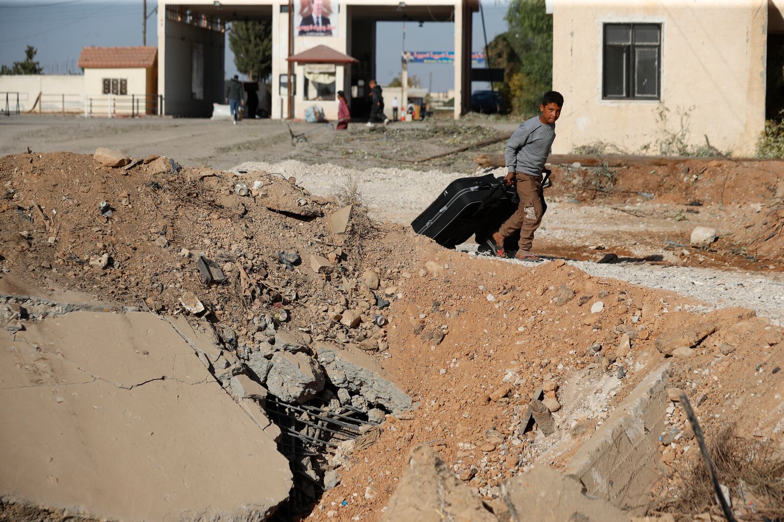 A Syrian boy fleeing the war in Lebanon carries his luggages as he passes through a crater caused by an Israeli airstrike, which blocks the road between the Lebanese and the Syrian crossing points, in Jousieh, Syria, Sunday, Oct. 27, 2024. (AP Photo/Omar Sanadiki)