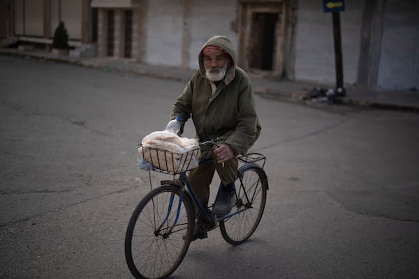 An elderly man transports a plastic bag with bread as he rides his bicycle on a street in an Alawite neighbourhood, in Homs, Syria, Thursday, Dec. 26, 2024. (AP Photo/Leo Correa)