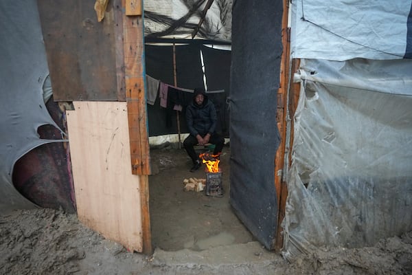 A man warms himself by a small fire inside a makeshift tent following overnight rainfall at the refugee tent camp for displaced Palestinians in Deir al-Balah, central Gaza Strip Tuesday, Dec. 31, 2024. (AP Photo/Abdel Kareem Hana)