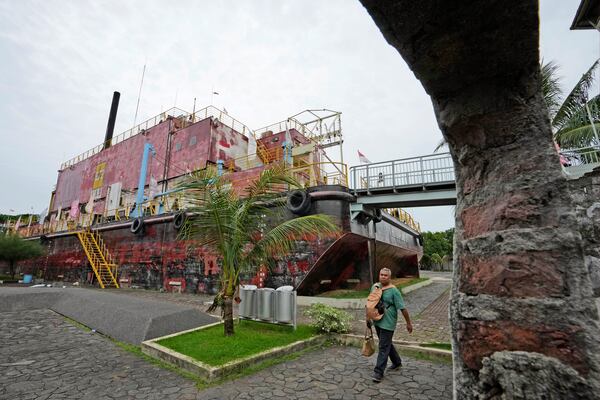 A man walks past a steel barge housing a diesel power generator swept ashore by the Indian Ocean tsunami in 2004 which is now preserved as a monument, in Banda Aceh, Indonesia, Saturday, Dec 14, Dec. 15, 2024. (AP Photo/Achmad Ibrahim)