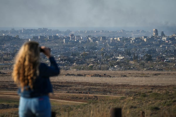 A woman uses binoculars to watch smoke rising following an explosion in the Gaza Strip as seen from southern Israel, Wednesday, Dec.18, 2024. (AP Photo/Ohad Zwigenberg)