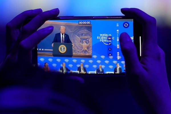 A woman takes pictures during a virtual speech of U.S. president Donald Trump at the Annual Meeting of World Economic Forum in Davos, Switzerland, Thursday, Jan. 23, 2025. (AP Photo/Markus Schreiber)