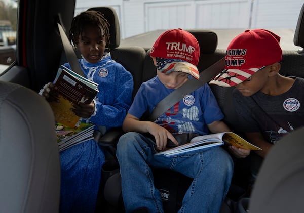 Gianna Young, 7, left, Isaac Young, 5, center, and Lucas Young, 8, look at books in the back seat of the truck for the trip to vote with adoptive parents Mike and Erin Young on Election Day, Tuesday, Nov. 5, 2024, in Sunbury, Ohio. (AP Photo/Carolyn Kaster)