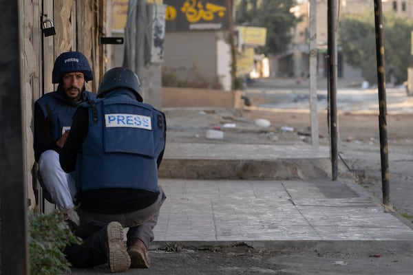 Journalists take cover from gunfire as Palestinian security forces mount a major raid against militants in the Jenin refugee camp in the Israeli-occupied West Bank, Monday, Dec. 23, 2024. (AP Photo/Majdi Mohammed)