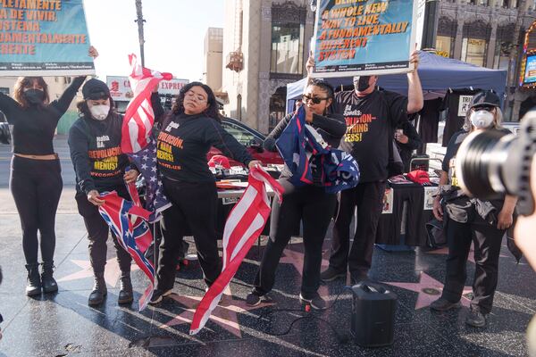 Members of the "Revcom Corps for the Emancipation of Humanity" stage a visual protest by a symbolic act of ripping the U.S. flag, the Confederate flag, and the Trump flag at Donald Trump's star on the Hollywood Walk of Fame in Los Angeles Monday, Jan. 20, 2025. (AP Photo/Damian Dovarganes)