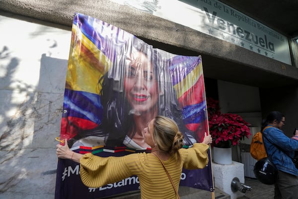 An opponent of Venezuelan President Nicolas Maduro hangs up an image of opposition leader Maria Corina Machado outside the Venezuelan embassy in Mexico City, Thursday, Jan. 9, 2024, a day before Maduro's inauguration for a third term. (AP Photo/Fernando Llano)