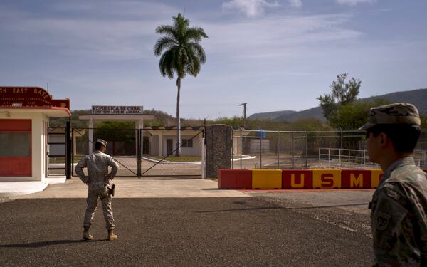 FILE - In this photo reviewed by U.S. military officials, an Army soldier, right, and a Marine stand in front of the gates that separate the Cuban side from the Guantanamo Bay U.S. Naval Base, June 6, 2018. (AP Photo/Ramon Espinosa, File)