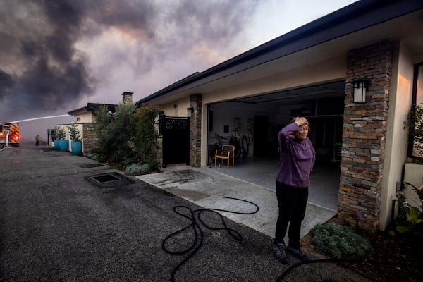 A resident stands in front of a garage as fire crews fight the Palisades Fire nearby in the Pacific Palisades neighborhood of Los Angeles, Tuesday, Jan. 7, 2025. (AP Photo/Ethan Swope)