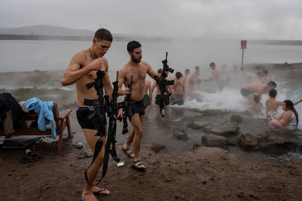 Israeli soldiers holding their weapons bathe with residents in a hot water pool coming from a drilling project which exposed a subterranean hydrothermal spring near Mount Bental in the Israeli-controlled Golan Heights, on the first day of the ceasefire between Israel and Hezbollah, Wednesday, Nov. 27, 2024. (AP Photo/Ohad Zwigenberg)