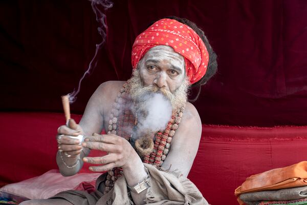 A Hindu holy man smokes marijuana at his makeshift living quarters at the confluence of the Ganges, the Yamuna and the mythical Saraswati rivers, a day before the official beginning of the 45-day-long Maha Kumbh festival, in Prayagraj, India, Sunday, Jan. 12, 2025. (AP Photo/Ashwini Bhatia)