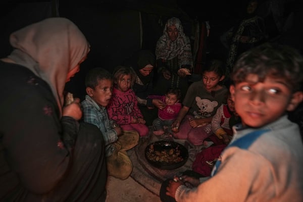 Amani Abu Zarada, fourth from left, feeds one of her children with fried zucchini made over a fire made of paper and cardboard scraps outside their tent in a camp in Khan Younis, Gaza Strip, Thursday, Dec. 19, 2024. (AP Photo/Abdel Kareem Hana)