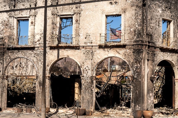 An American flag hangs behind a commercial building destroyed by the Palisades Fire in the Pacific Palisades neighborhood of Los Angeles, Sunday, Jan. 12, 2025. (AP Photo/Noah Berger)