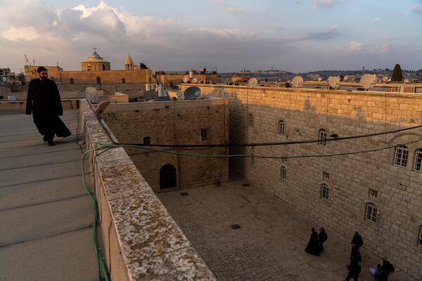 An Armenian Christian deacon walks on a roof terrace near St. James Cathedral, background, at the Armenian quarter in Jerusalem, Thursday, Nov. 21, 2024. (AP Photo/Francisco Seco)