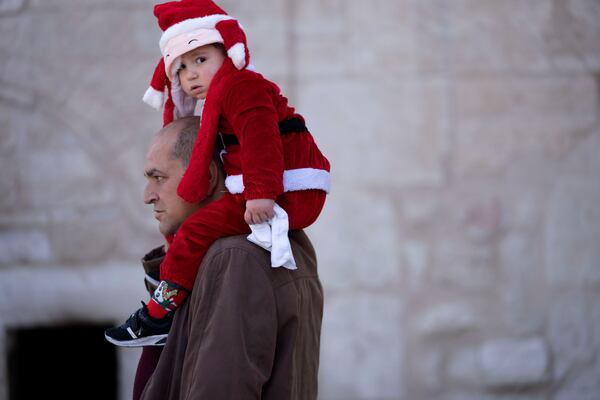 Anton Nakle carries his three year-old son, David, dressed in a tiny Santa Claus suit, into the Church of the Nativity, where Christians believe Jesus Christ was born, in the West Bank city of Bethlehem, on Christmas Eve for Orthodox Christians, Monday, Jan. 6, 2025. (AP Photo/Maya Alleruzzo)